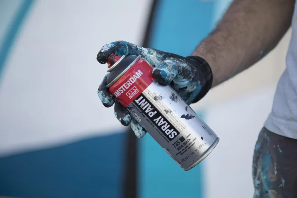 Main tachée de peinture tenant une bombe Amsterdam Spray Paint, fond bleu — Royal Talens
